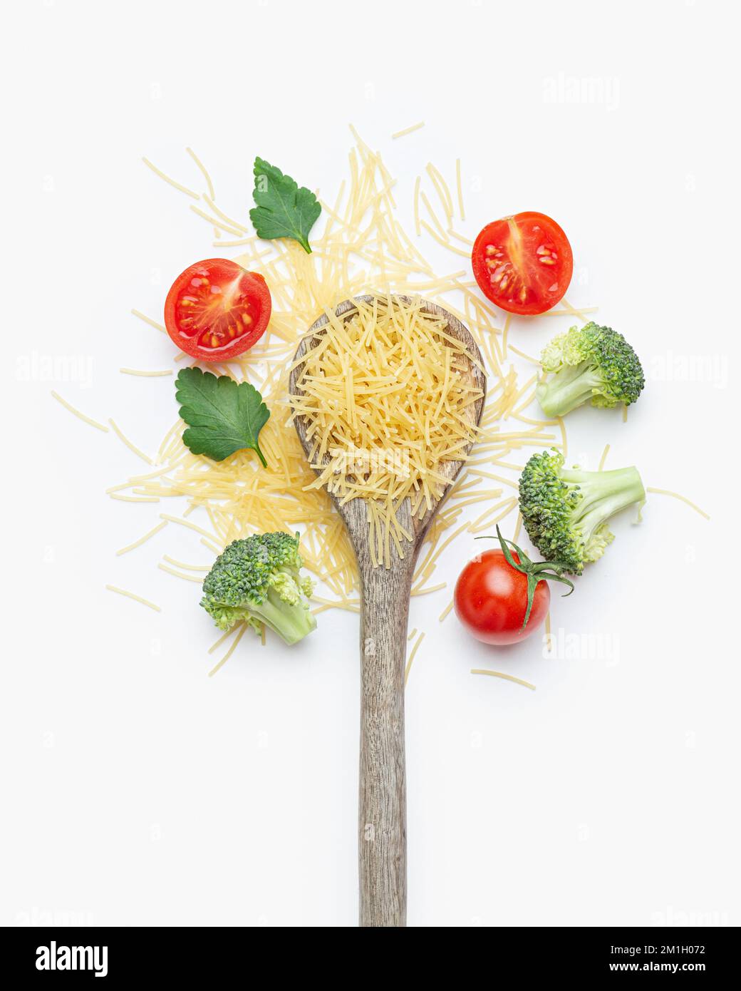 Pâtes crues aux tomates, brocoli, persil et parmesan dans une cuillère en bois sur fond blanc Banque D'Images