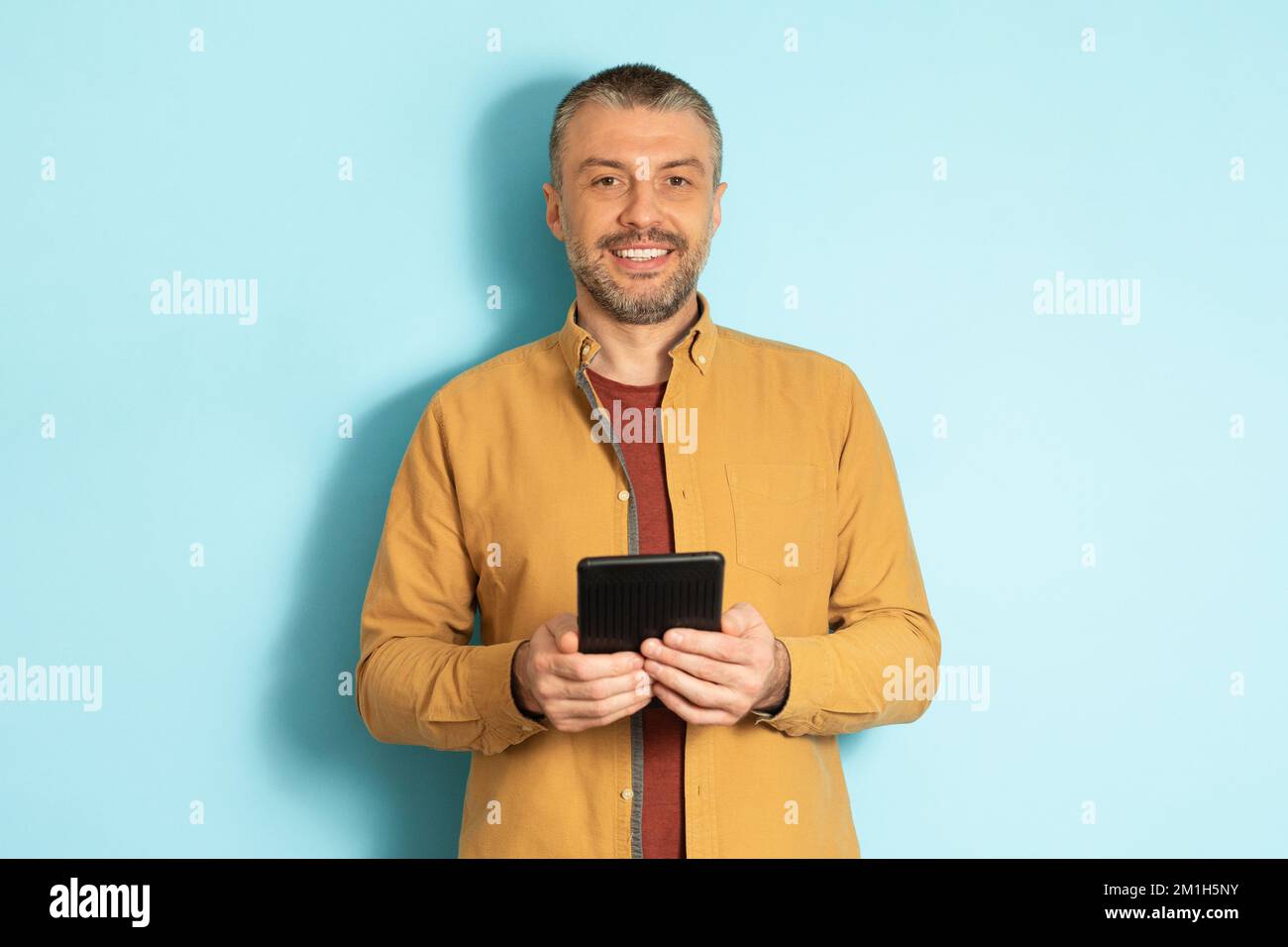 Concept de personnes et de technologie. Portrait d'un homme caucasien mature tenant et utilisant une tablette debout sur fond bleu Banque D'Images