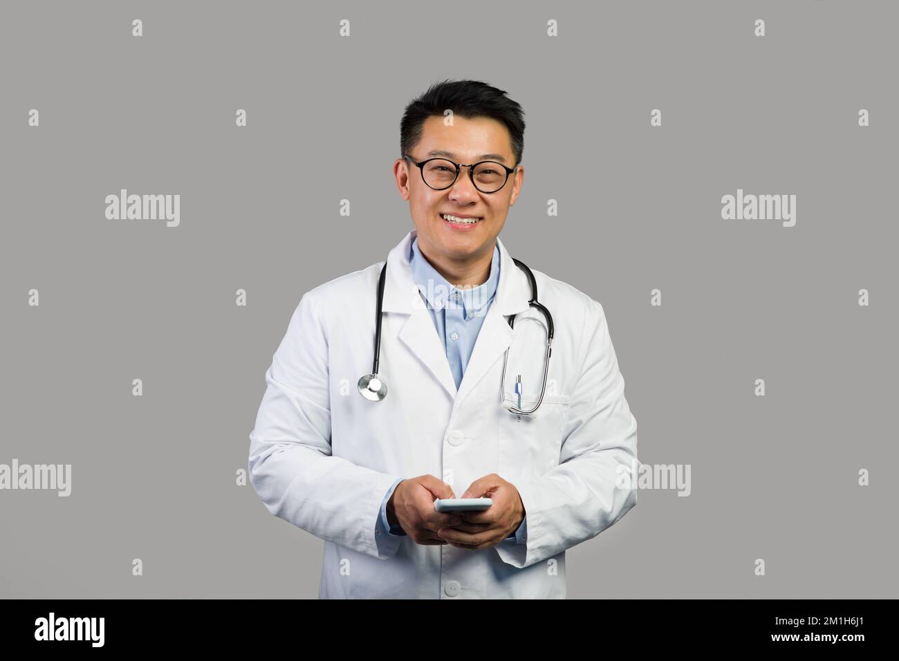 Bon thérapeute chinois pour adultes en manteau blanc et lunettes avec stéthoscope utiliser un smartphone pour le travail Banque D'Images