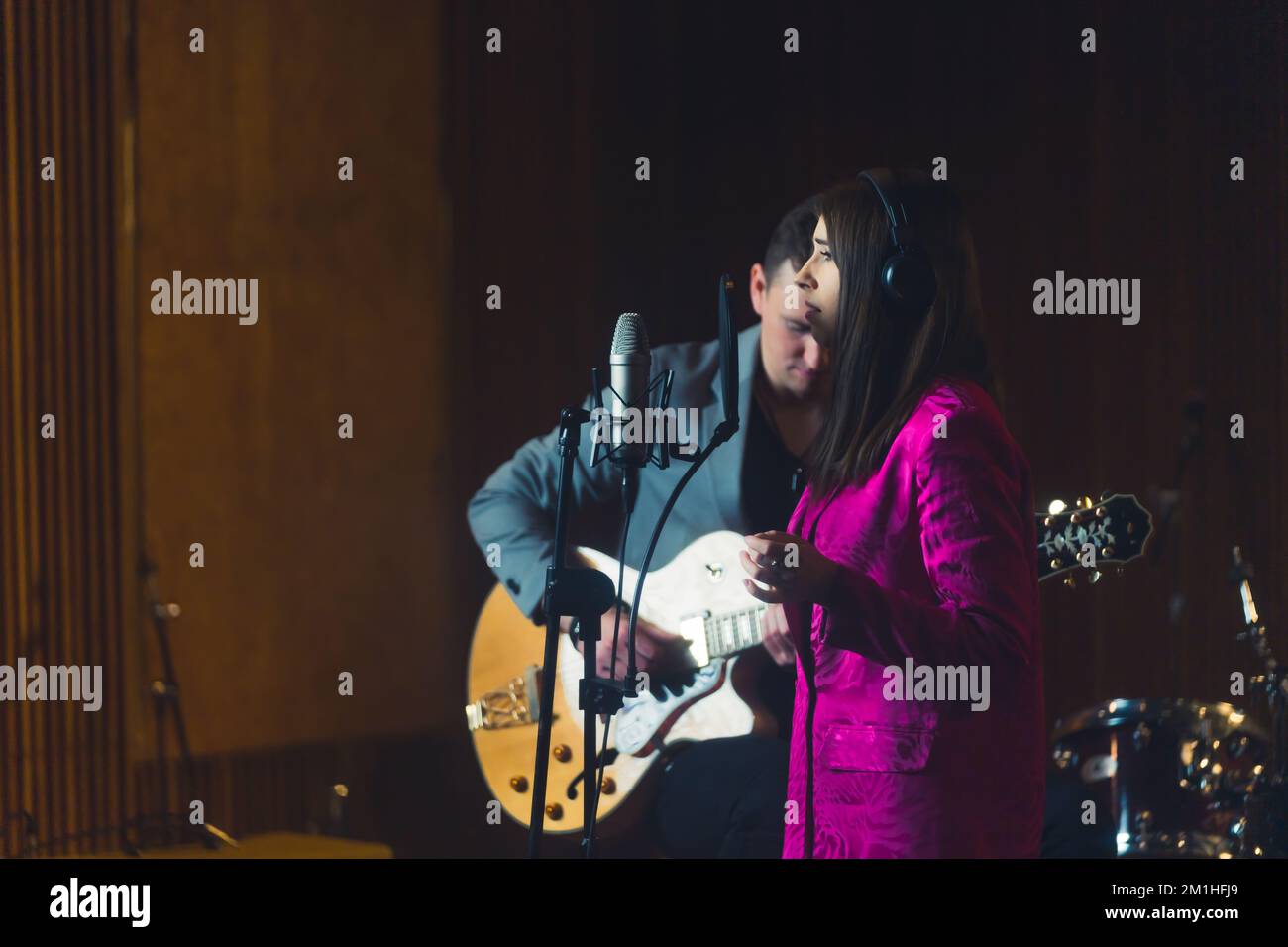 Prise de vue en intérieur moyenne d'un groupe enregistrant une nouvelle chanson. Jeune femme caucasienne chantant dans un microphone d'enregistrement. Guitariste en arrière-plan. Photo de haute qualité Banque D'Images