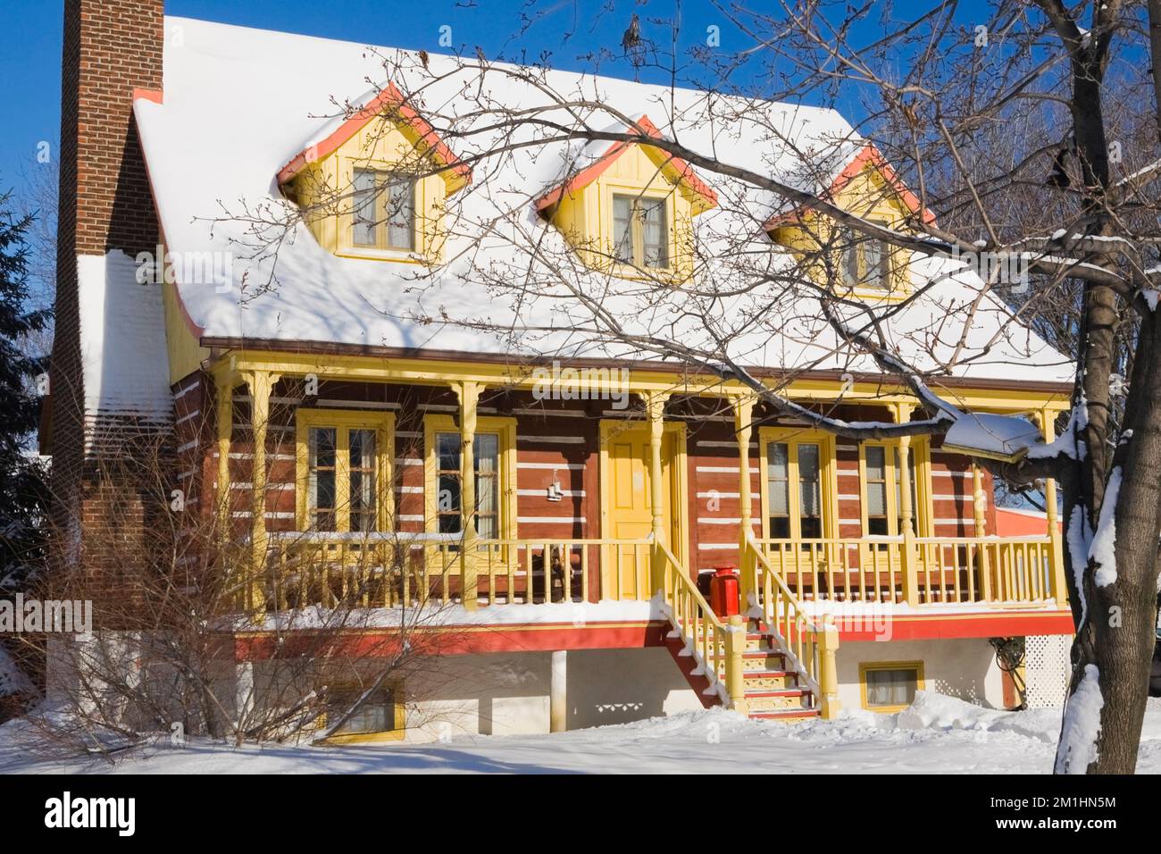 1978 réplique construite de l'ancien 1800s jaune avec garniture orange maison en rondins de style Canadiana en hiver. Banque D'Images