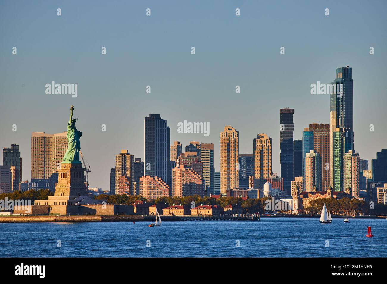 Statue de la liberté avec gratte-ciel entourant les eaux en lumière dorée Banque D'Images