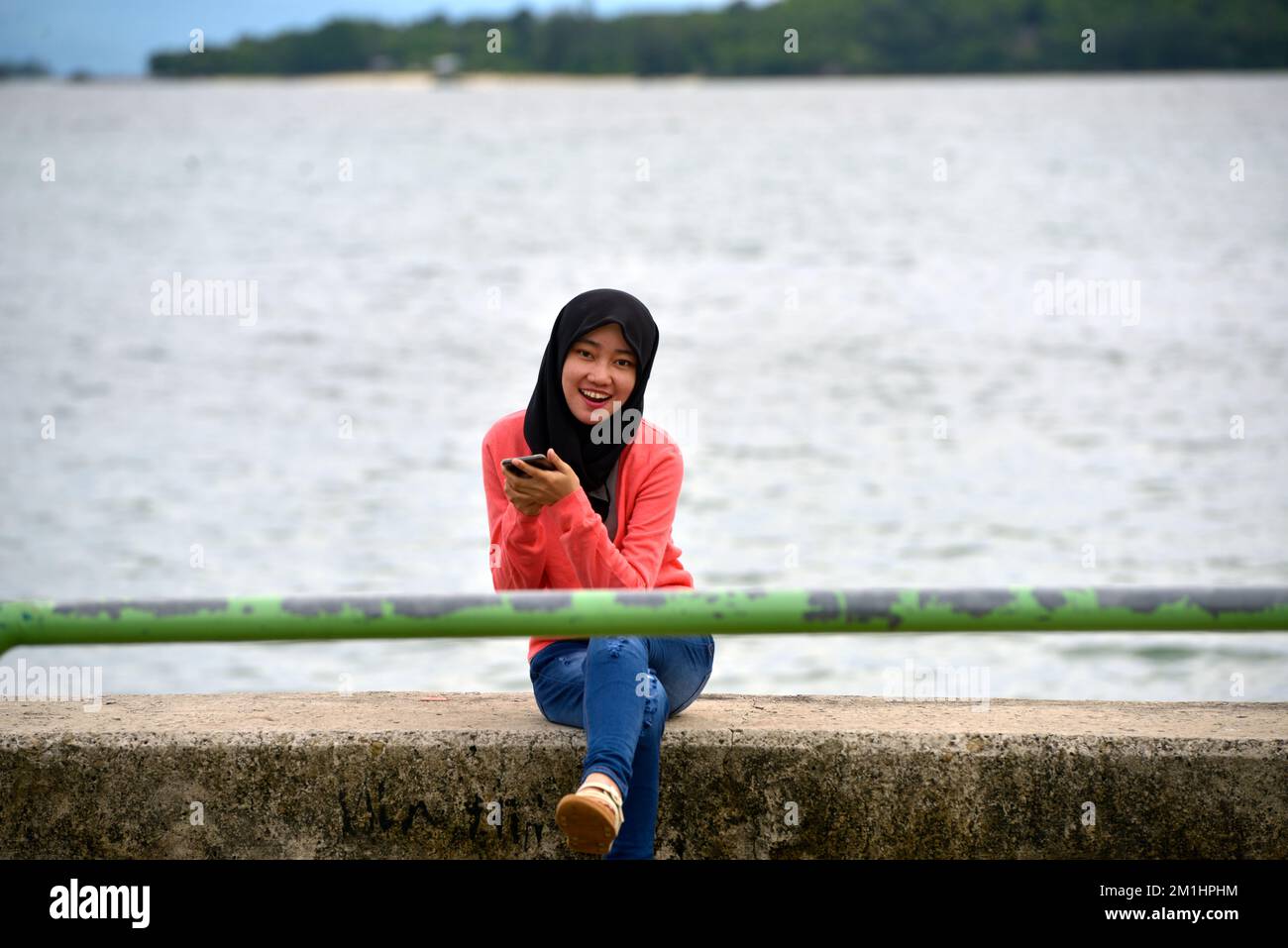 Une jeune fille autochtone de Rungus tenant son téléphone mobile tout en étant assise sur le quai à Kudat, Sabah, Bornéo, Malaisie. Banque D'Images
