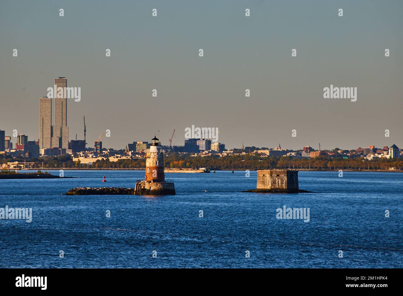 Robbins Reef Lighthouse à New York avec lumière dorée et ville industrielle derrière Banque D'Images