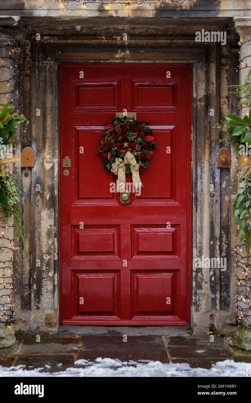 Couronne sur une porte rouge. Traditionnel, à l'ancienne. Décorations de Noël festives dans la rue lors d'une journée d'hiver avec de la neige Banque D'Images