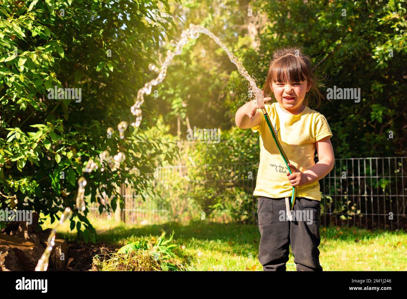 Bonne petite fille jouant avec un tuyau de jardin. Enfant d'âge préscolaire s'amuser avec les arbres et les plantes dans le jardin domestique Banque D'Images