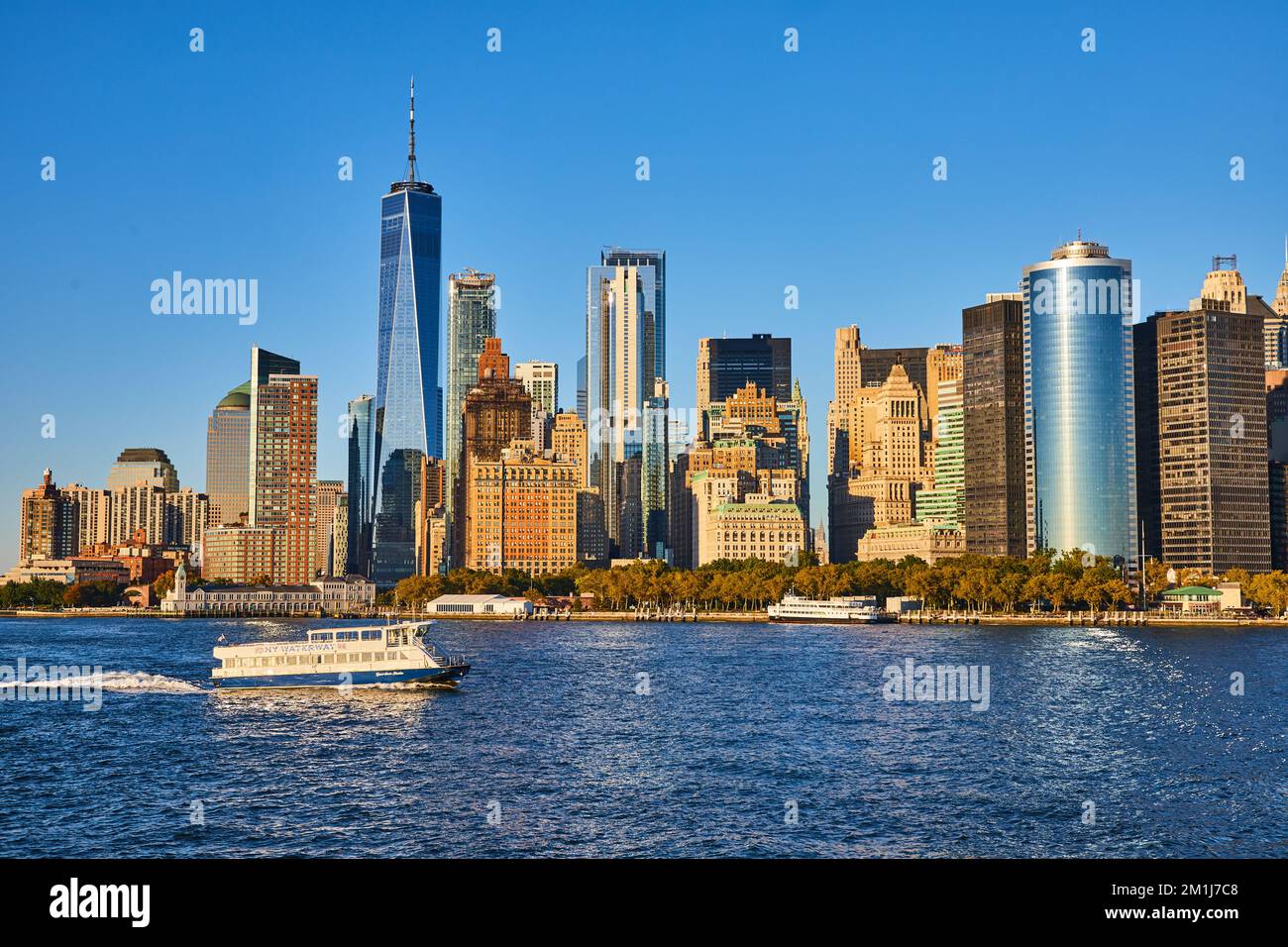 Ferry traversant les gratte-ciel du sud de Manhattan depuis l'eau avec lumière dorée sur les gratte-ciel Banque D'Images
