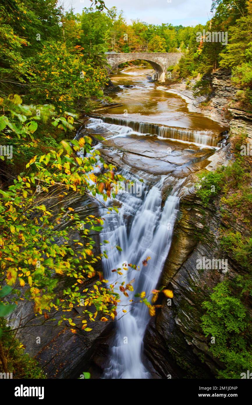 Cascade dans des gorges profondes avec feuillage d'automne, forêt, et pont voûté en pierre en arrière-plan Banque D'Images