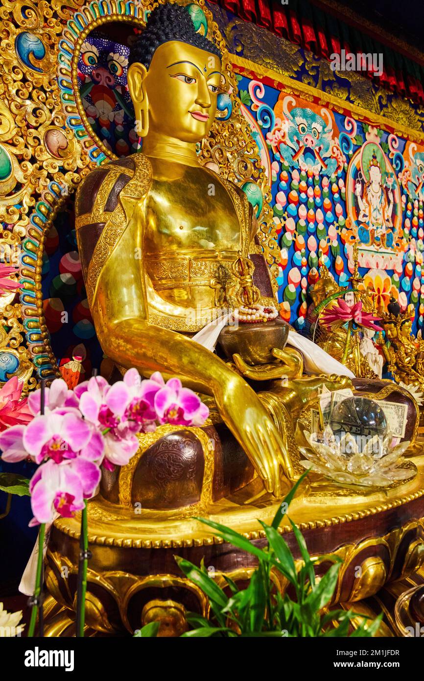Statue de Bouddha ornée d'or dans un sanctuaire avec orchidées roses Banque D'Images