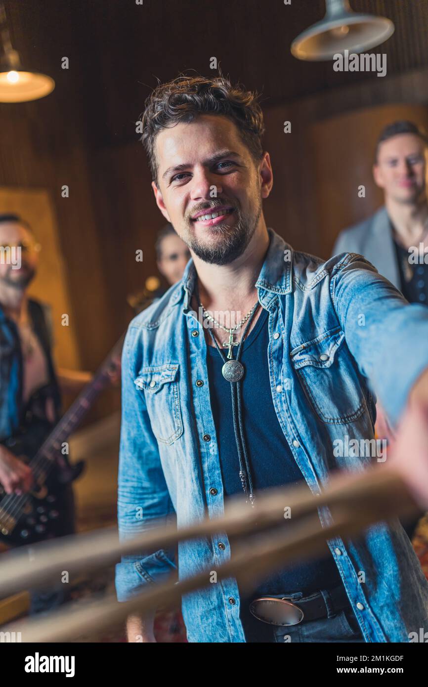 Prise de vue verticale en intérieur d'un batteur montrant ses bâtons à la caméra. Souriant homme caucasien adulte moyen dans une veste en denim comme un batteur de groupe. Photo de haute qualité Banque D'Images