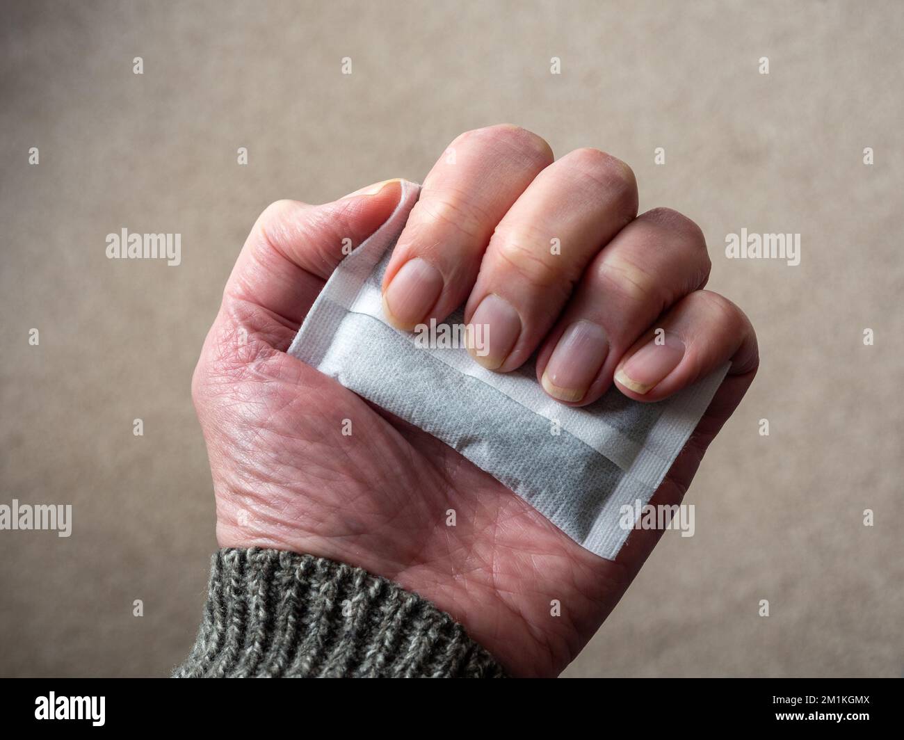 Homme senior tenant la main d'un chauffe-main jetable à air activé à l'intérieur ; une alternative au chauffage central pendant la crise énergétique, Royaume-Uni Banque D'Images