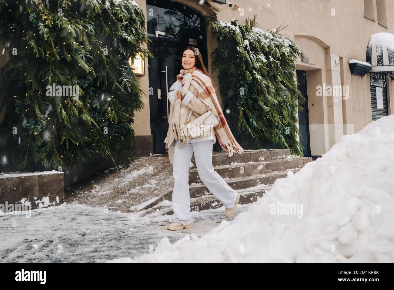 Une fille aux cheveux longs dans un foulard et avec un sac à main blanc  descend dans la rue en hiver Photo Stock - Alamy