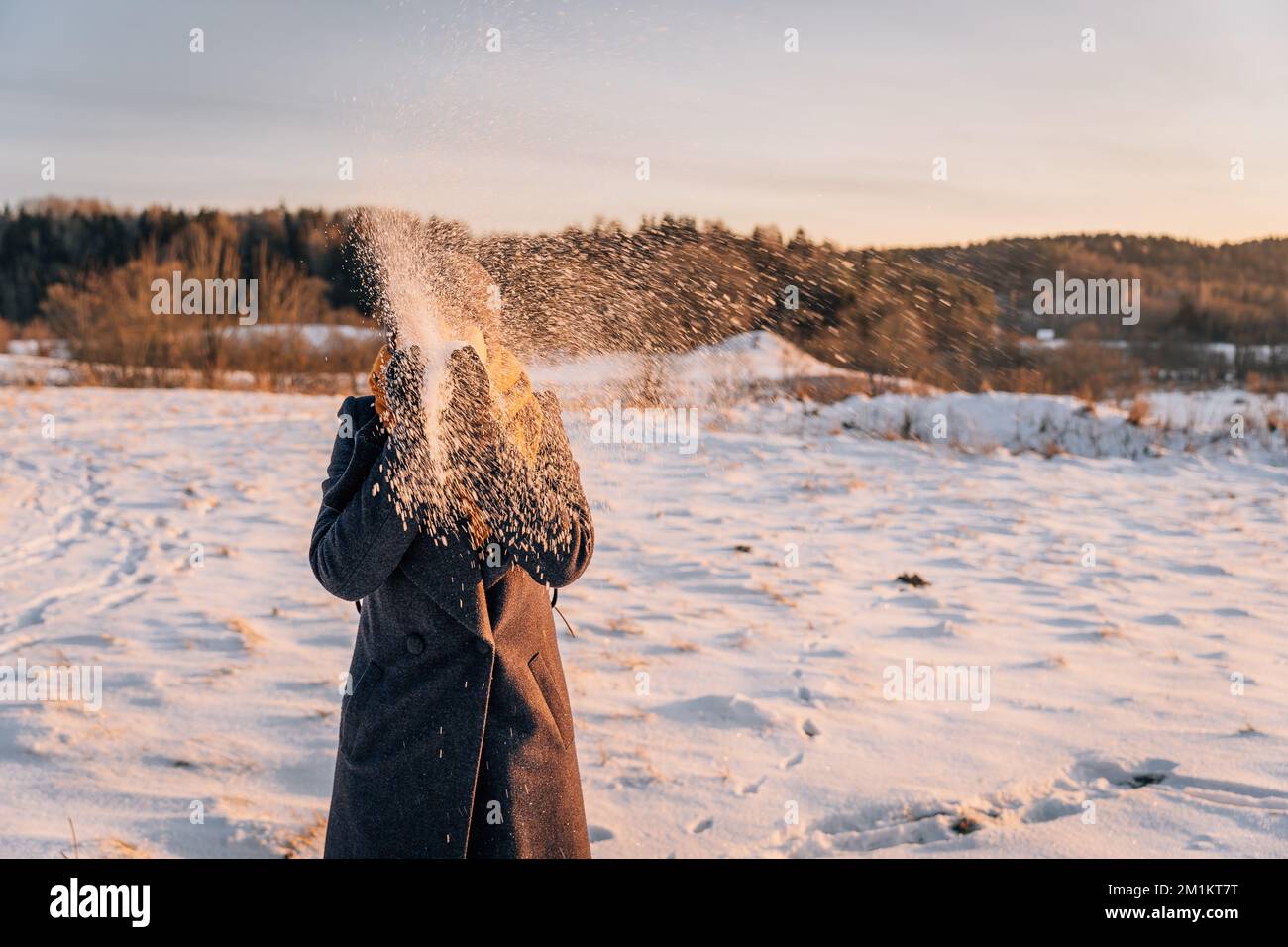 Une femme au visage obscurci jette de la neige avec ses mains dans un champ enneigé Banque D'Images
