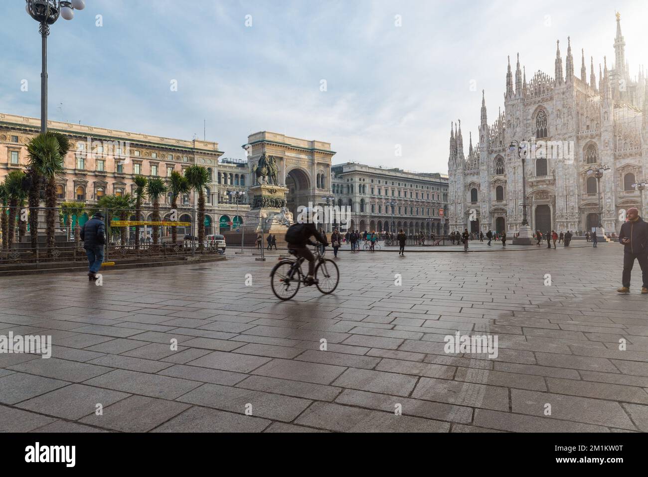 Milan au lever du soleil. Place Duomo avec le Duomo de Milan sur la droite et la galerie Vittorio Emanuele II derrière le cycliste Banque D'Images