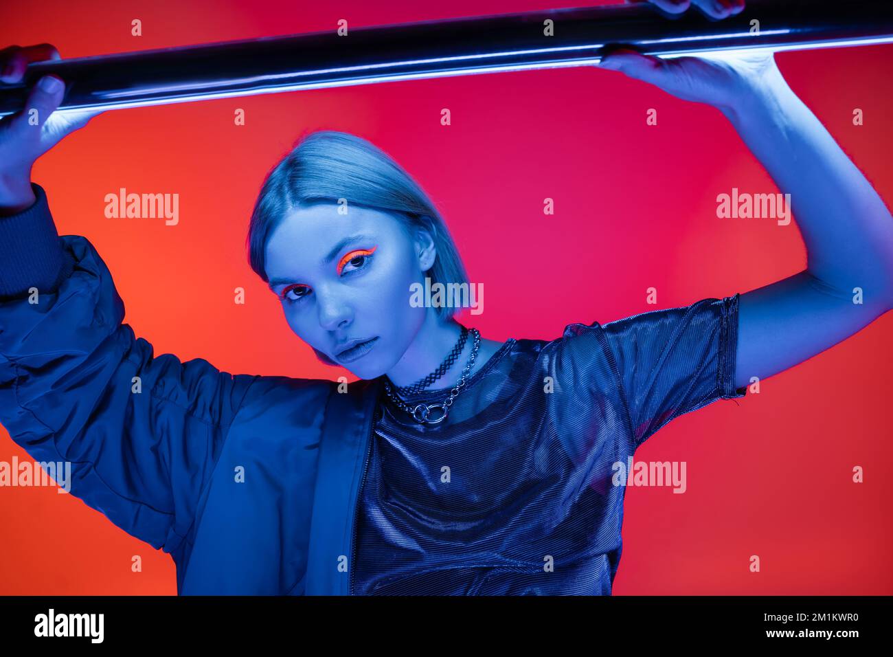 jeune et élégante femme regardant l'appareil photo dans la lumière bleue de la lampe néon sur fond corail et rose, image de stock Banque D'Images