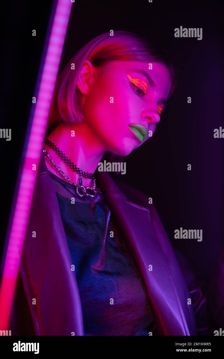 vue à angle bas de la femme avec maquillage lumineux dans la lumière néon violet sur fond sombre, image de stock Banque D'Images