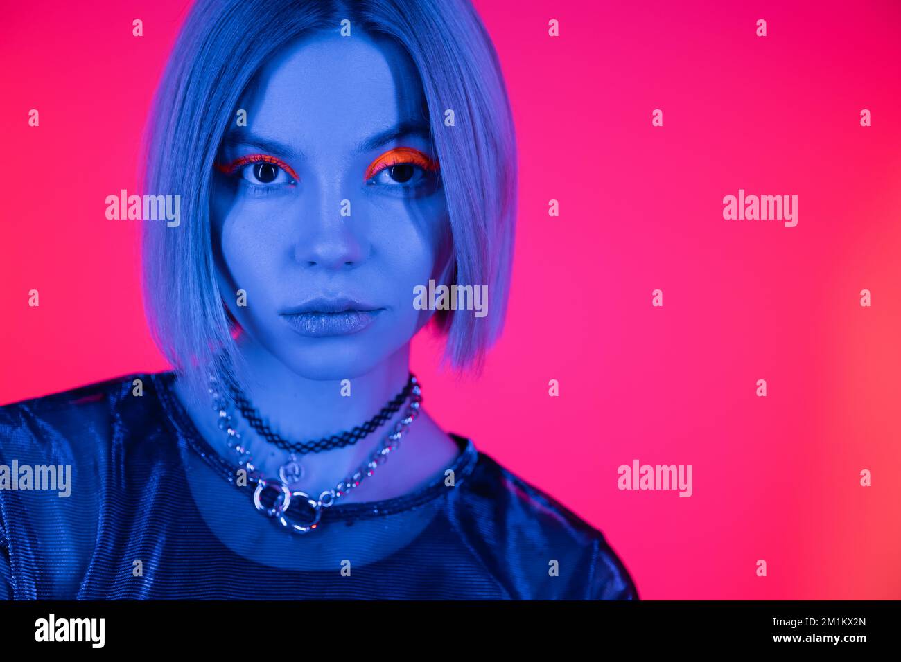 portrait de la femme tendance avec colliers et maquillage fluorescent dans lumière bleue néon sur fond rose profond, image de stock Banque D'Images