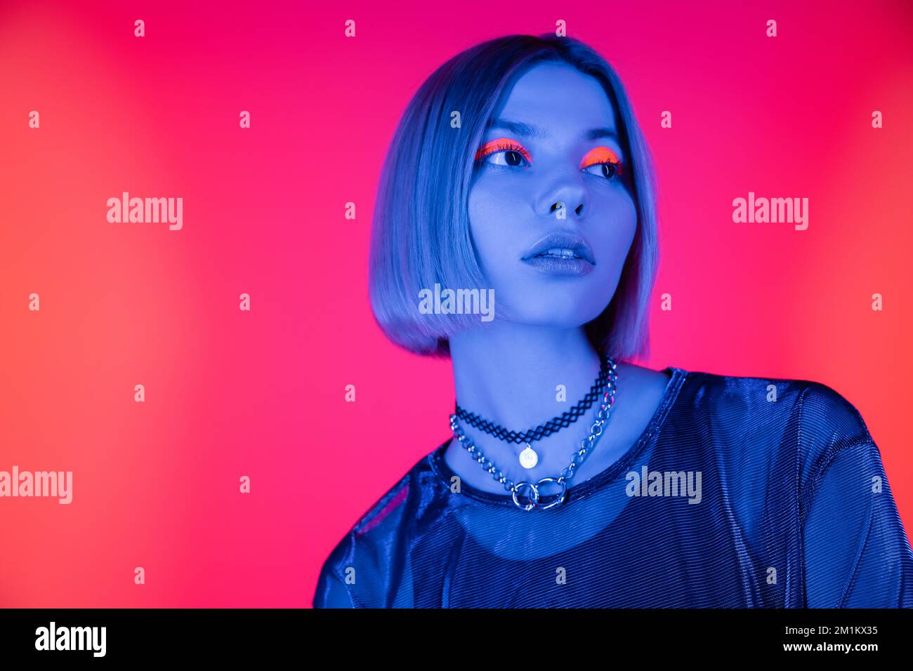 femme à la mode avec maquillage néon regardant loin dans la lumière bleue sur fond rose corail, image de stock Banque D'Images