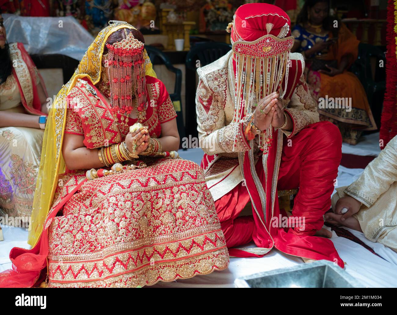 Lors d'un mariage hindou, la mariée et le marié sont assis avec leurs mains jointes et portant des coiffures de sehra. À Queens, New York. Banque D'Images