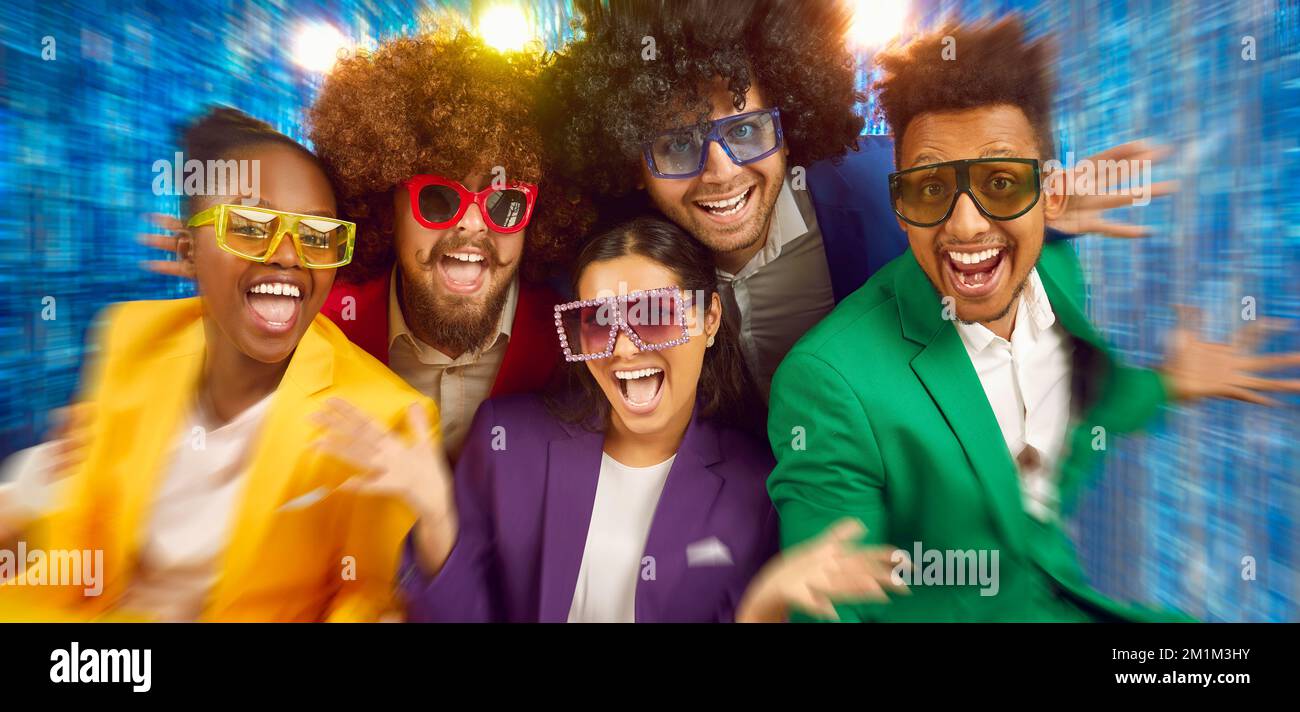 Portrait des gens en train de rire dans des lunettes de soleil de style disco, costumes colorés sur fond bleu flou. Banque D'Images