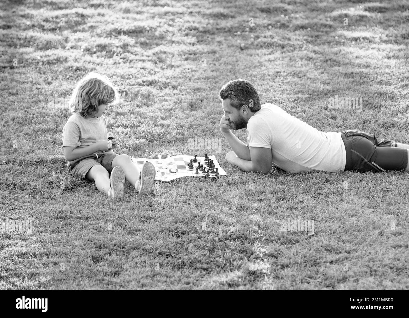 famille heureuse de père et fils enfant jouant aux échecs sur l'herbe verte dans le parc extérieur, échecs Banque D'Images
