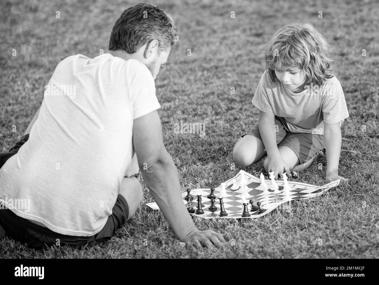 bonne famille de père homme et fils garçon jouant aux échecs sur l'herbe verte dans le parc extérieur, adversaire Banque D'Images