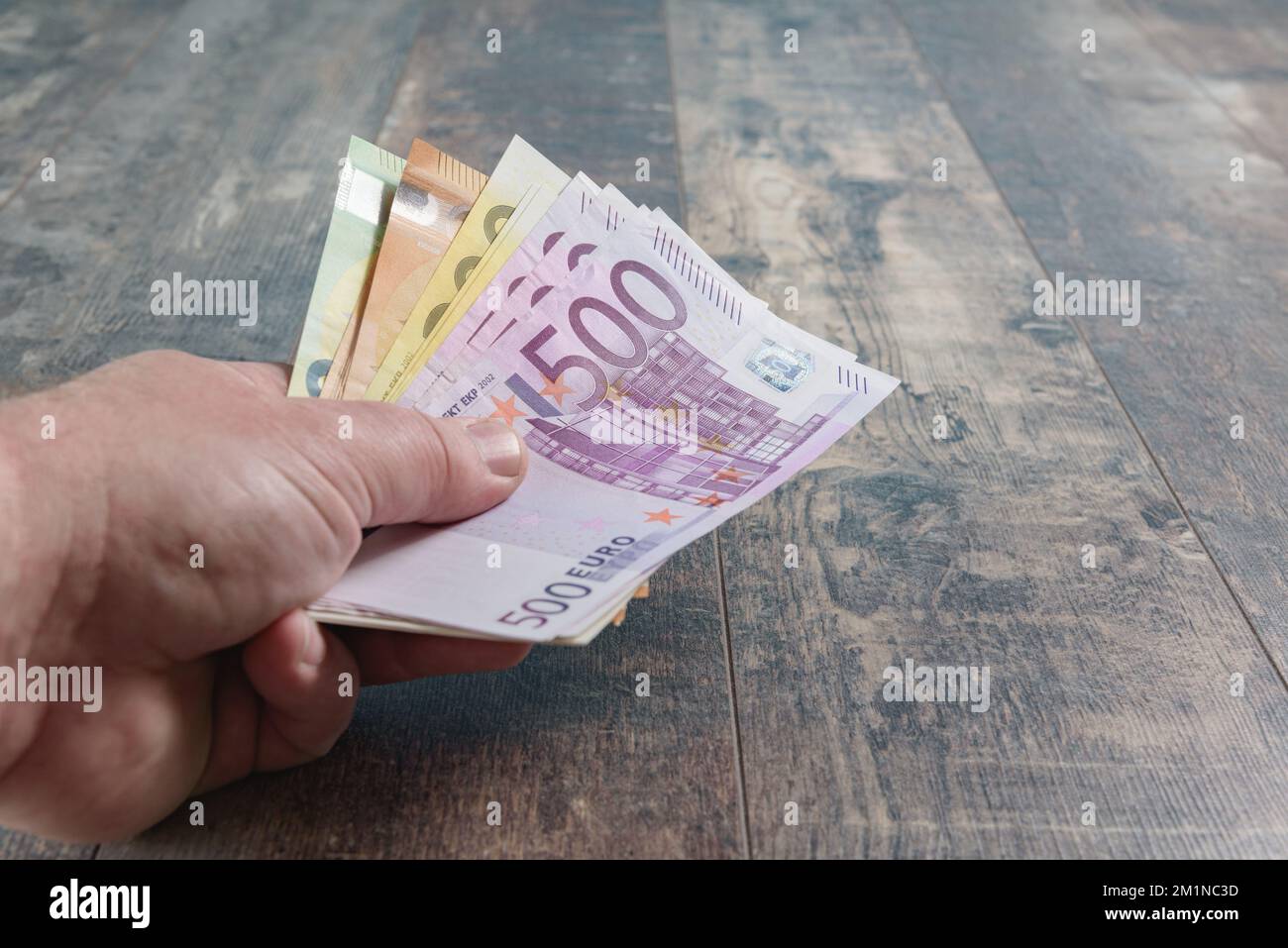 Montant des grands billets en euros dans la main masculine. Gros plan sur un fond rustique en bois Banque D'Images