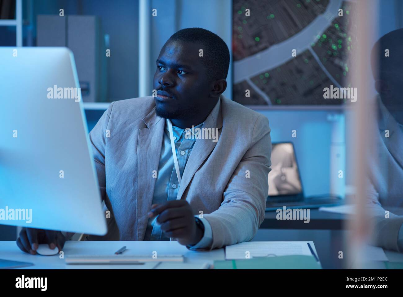 Portrait d'homme noir travaillant dans un centre de sécurité et utilisant un ordinateur, scène de ton bleu Banque D'Images