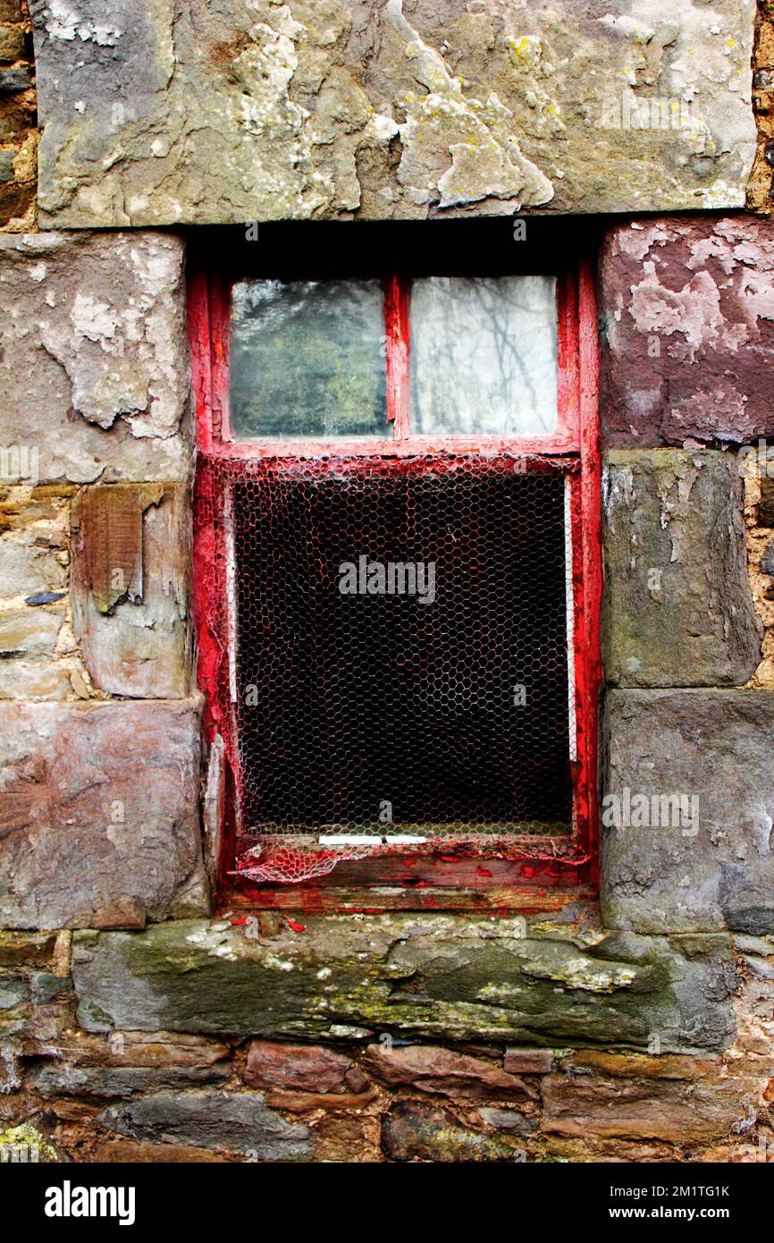 Une fenêtre en bois peint en rouge avec des intempéries dans un mur de chalet en ardoise avec des intempéries. Banque D'Images