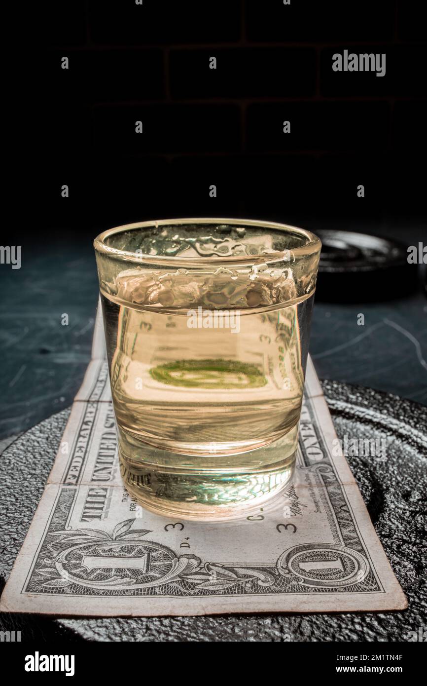 Un cliché vertical d'un verre de tequila sur un billet de banque d'un dollar sur une plaque métallique Banque D'Images