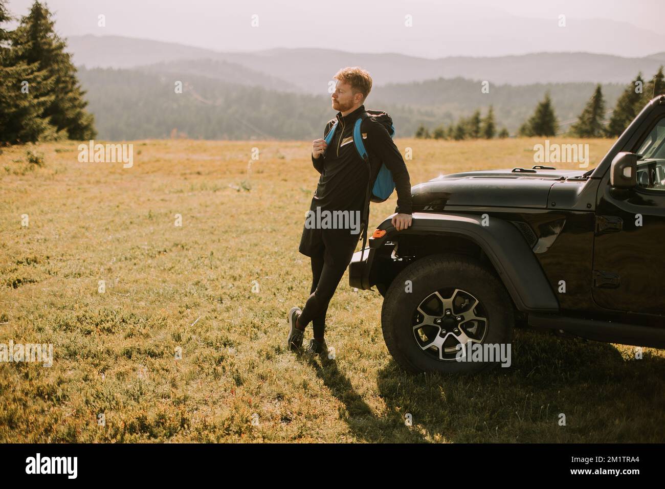 Beau jeune homme se reposant près du capot de véhicule de terrain à la campagne Banque D'Images