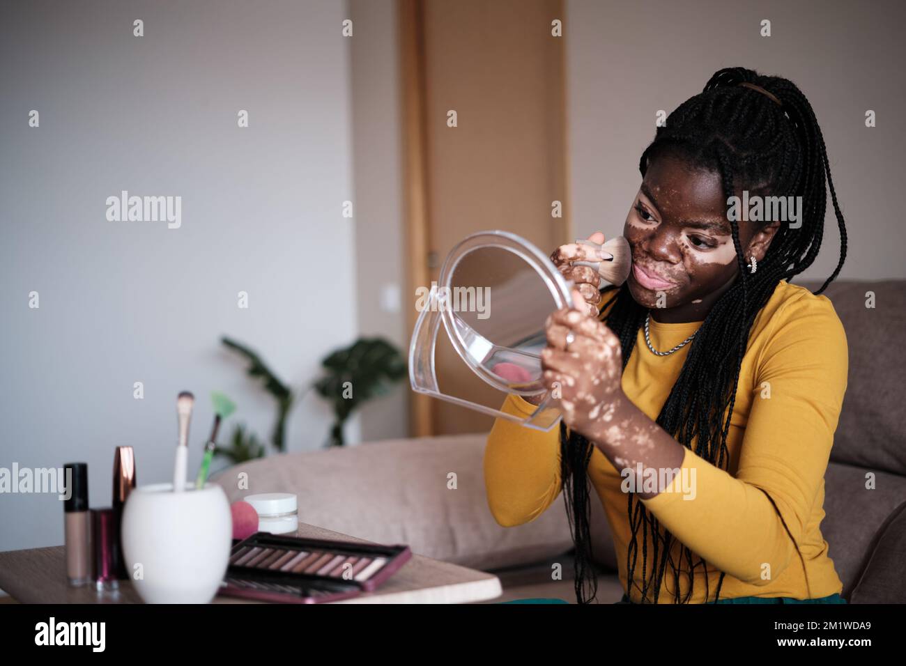 Femme noire positive appliquant le maquillage à la maison Banque D'Images