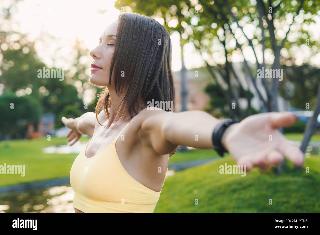Femme faisant du yoga au parc en appréciant la nature pendant un exercice de respiration, étirant les bras. Un mode de vie actif et sain. Exercices d'étirement du matin et Banque D'Images