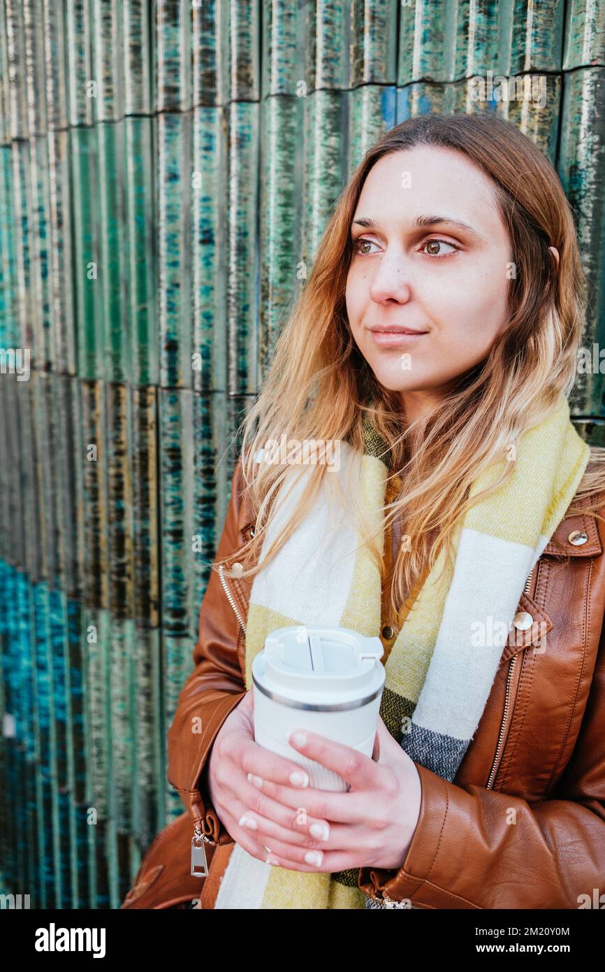 Portrait vertical d'une jeune femme attirante penchée sur un mur. Elle tient une tasse à café à emporter Banque D'Images