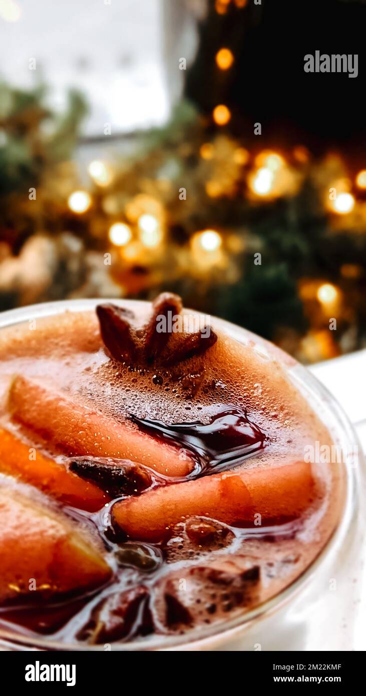 Vin chaud de Noël sur fond flou de lumières vives. Boisson chaude traditionnelle du nouvel an à base de vin rouge, d'orange, de cannelle, de pommes et d'épices anis étoilé. Cocktail de Noël. Mise au point sélective Banque D'Images