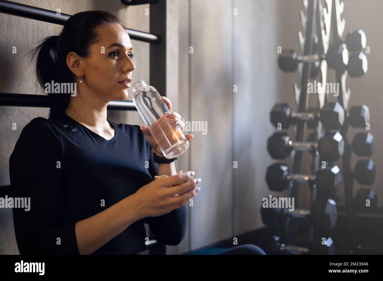 Femme brunette fatiguée relaxant de boire bouteille d'eau à la salle de gym après l'entraînement profiter de la perte de poids bien-être Banque D'Images
