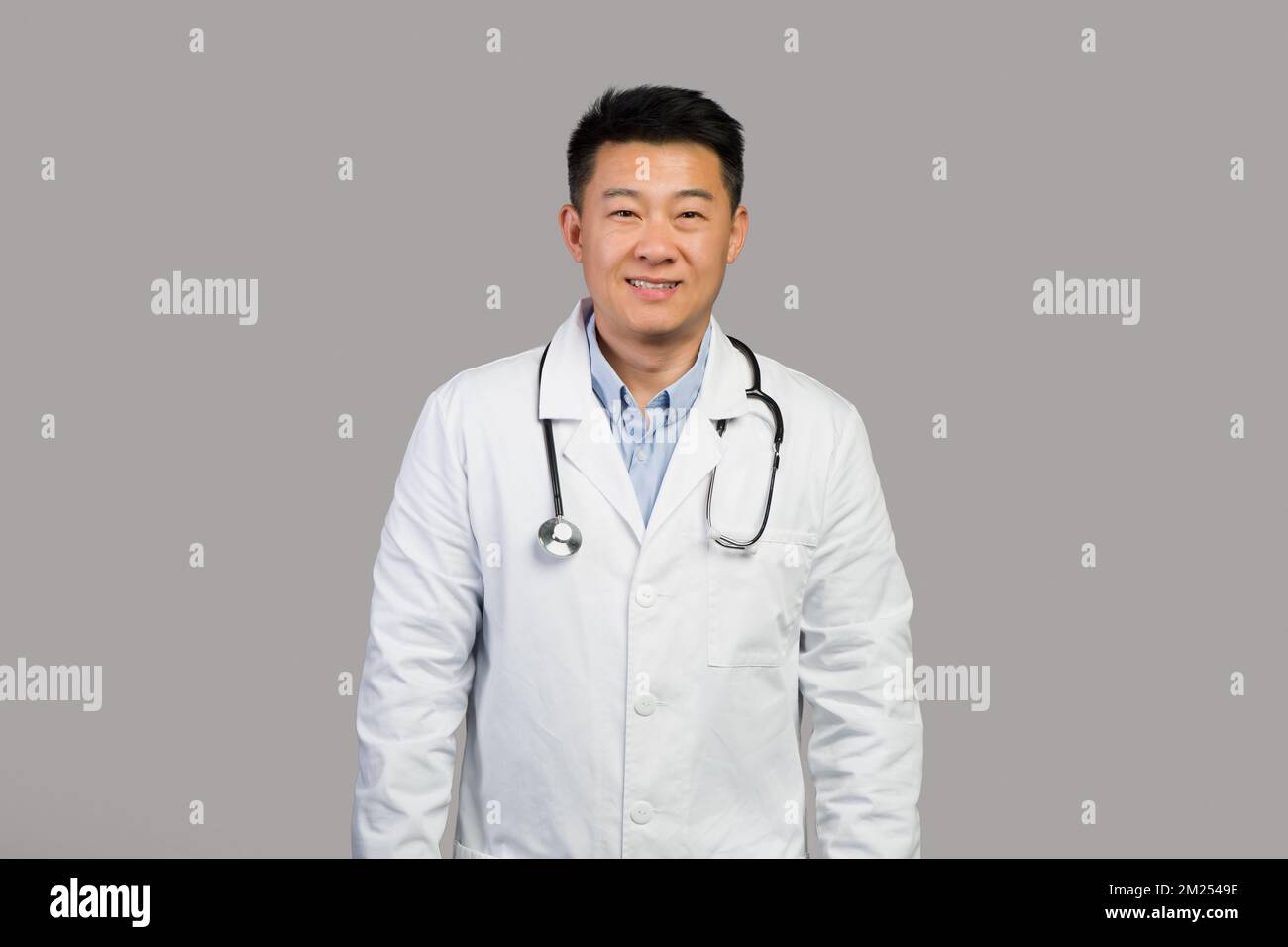 Souriant confiant et charmant homme chinois mature thérapeute en manteau blanc avec stéthoscope Banque D'Images
