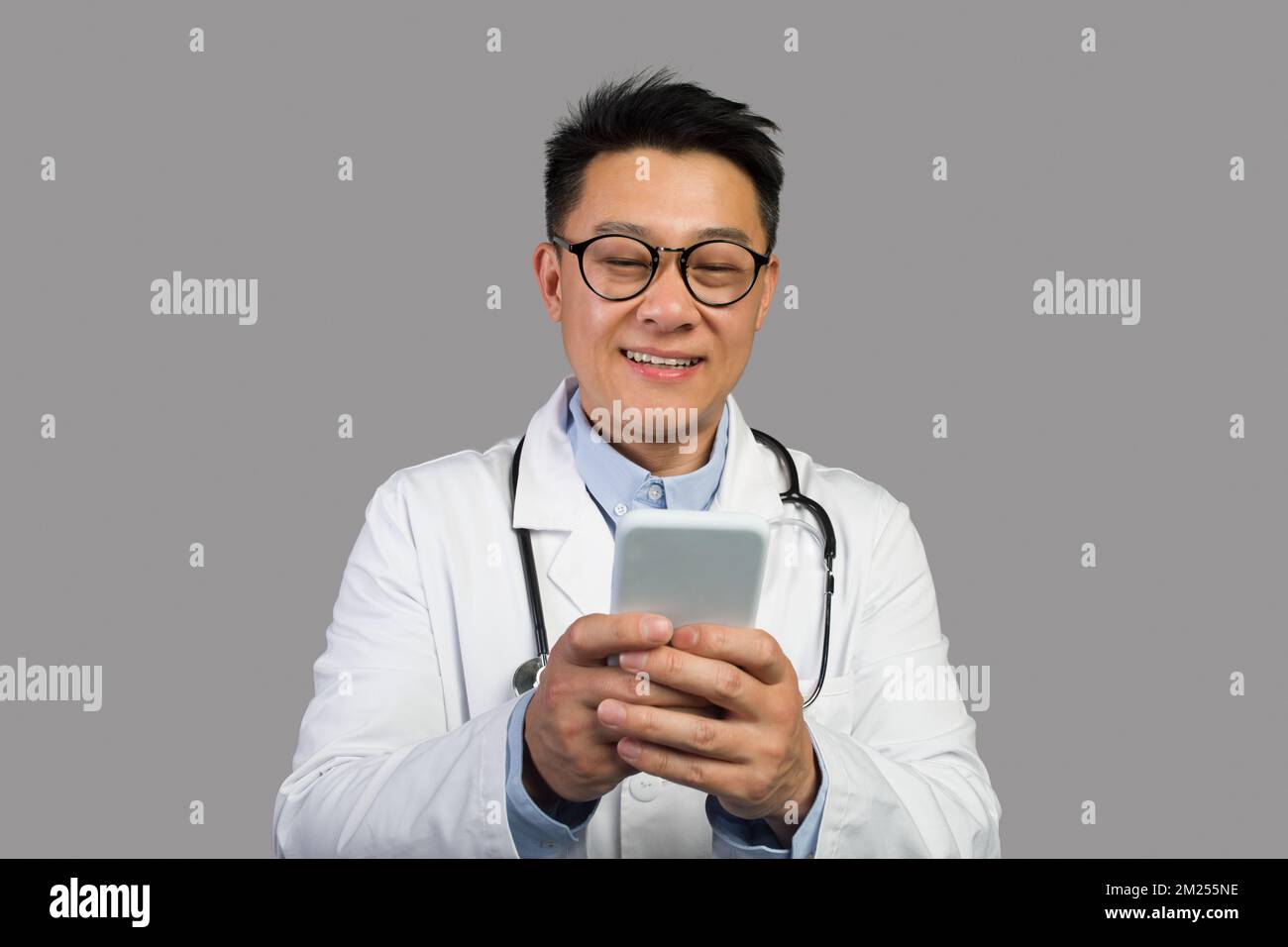 Gai adulte japonais thérapeute masculin en manteau blanc et des lunettes avec stéthoscope dactylographiant sur le téléphone Banque D'Images