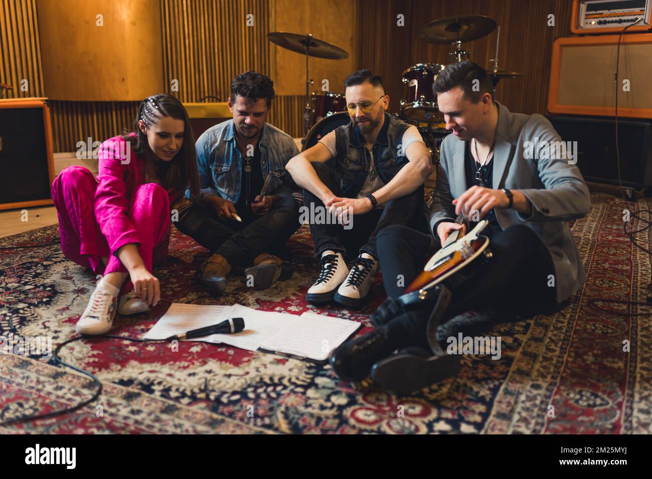 Vue panoramique sur un chanteur et trois autres musiciens assis sur un tapis coloré et sur un système d'écriture musicale. Intérieur du studio d'enregistrement. Photo de haute qualité Banque D'Images