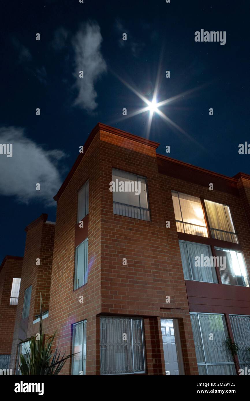 Une superbe photographie nocturne d'une maison en briques avec lumières allumées et une nuit étoilée avec pleine lune comme une étoile. Banque D'Images