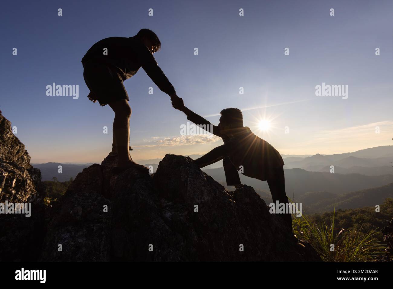 Silhouette de la main d'aide entre deux grimpeurs. Couple de randonnée aider l'autre silhouette dans les montagnes avec la lumière du soleil. Les hommes qui aident à tirer les gens vers le haut f Banque D'Images