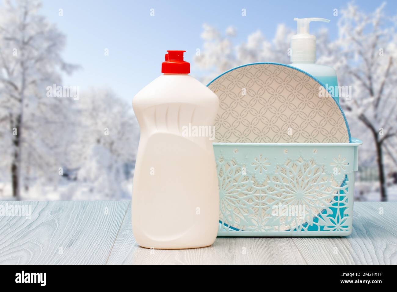 Bouteilles de liquide vaisselle, assiette dans le panier avec l'hiver sur fond. Banque D'Images