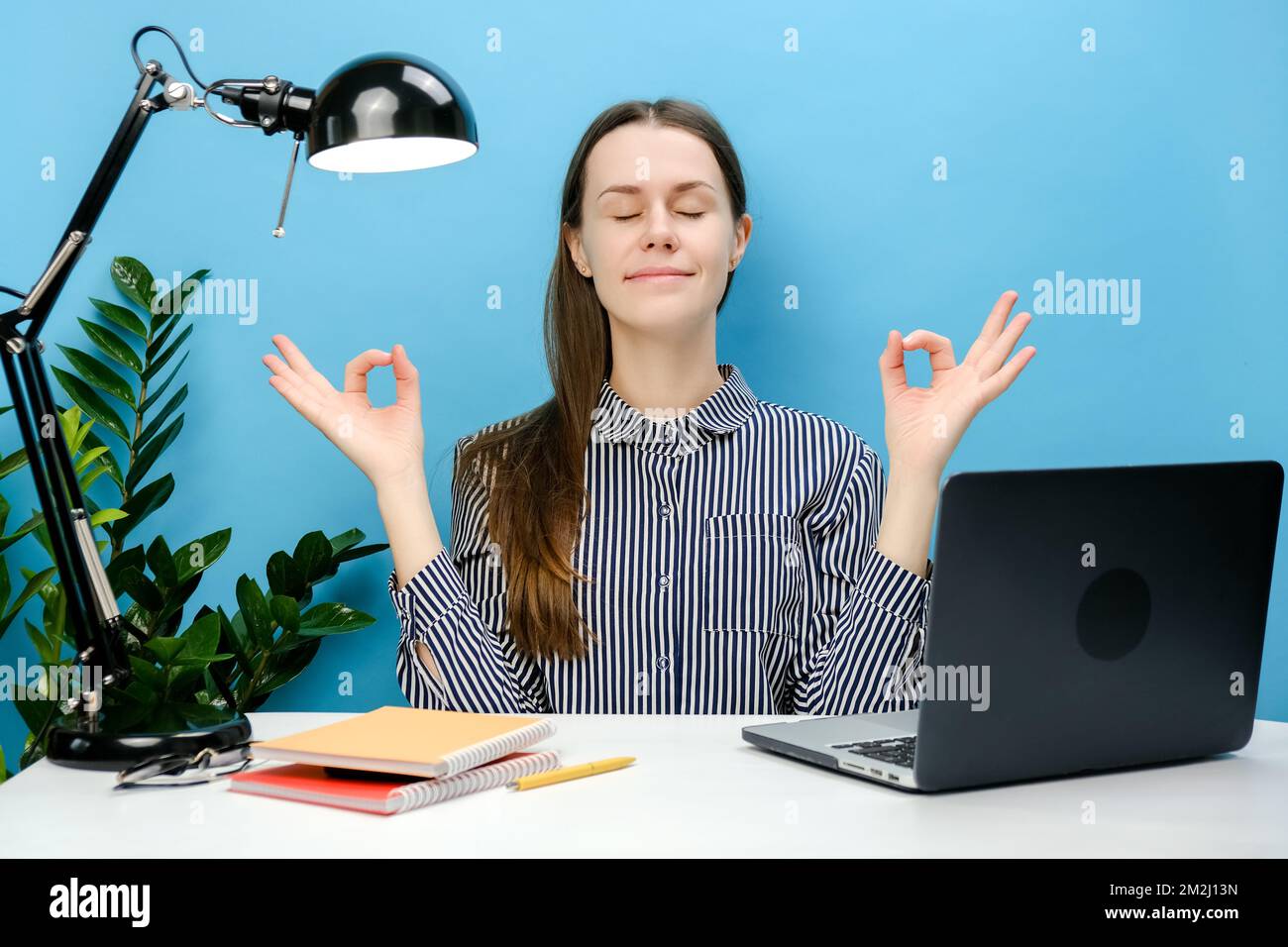 Portrait d'un employé réussi, jeune femme s'assoit au bureau blanc avec ordinateur portable tenir les mains dans le yoga om geste détendre méditer essayer de se calmer, p Banque D'Images