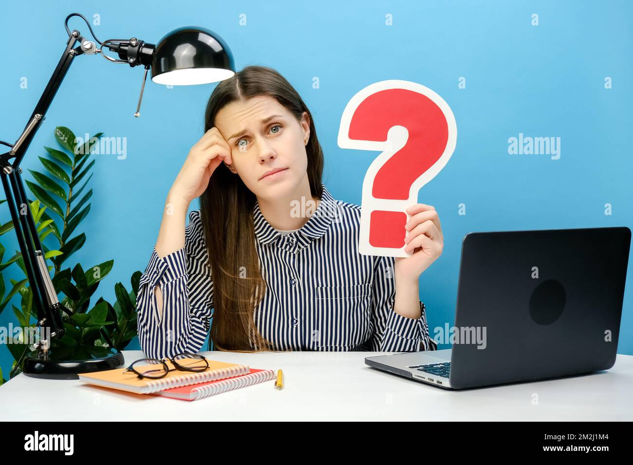 Jeune femme pensive 20s en chemise travail assis au bureau blanc pc portable tenant le signe d'interrogation rouge, posant isolé sur la couleur bleue Banque D'Images