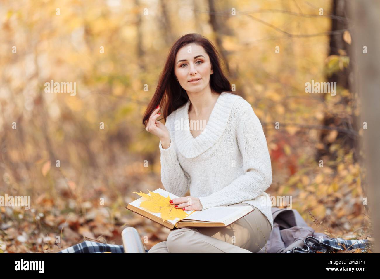 Vue latérale de la femme brune heureuse en lunettes de vue assise sur le banc et livre de lecture dans le parc. Photo de haute qualité Banque D'Images