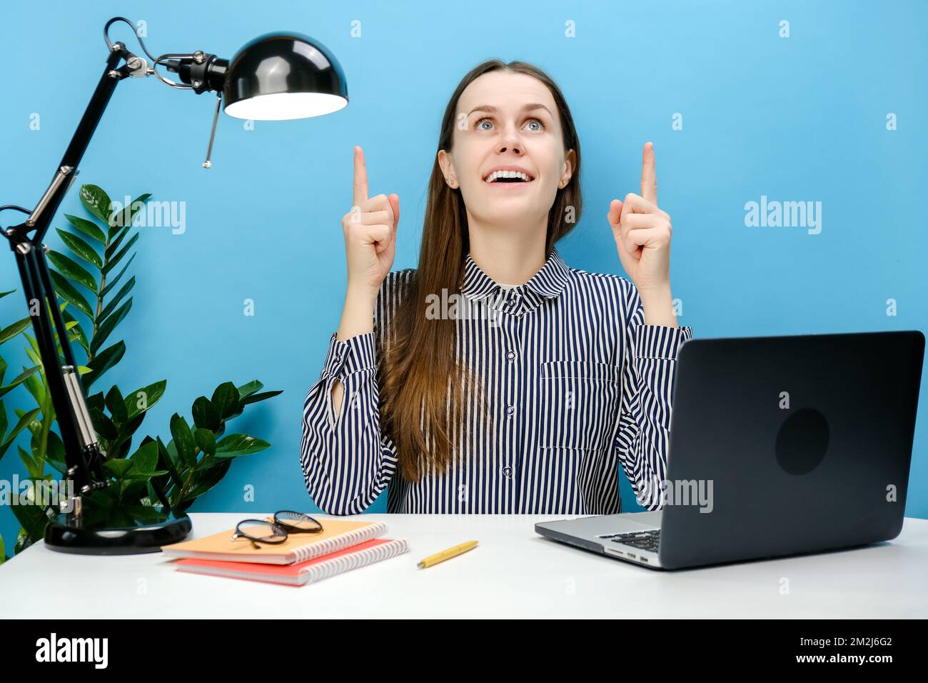 Une femme d'affaires enthousiaste et réussie dans un chemise décontracté, assis au bureau blanc avec un ordinateur portable point index tête sur l'espace de copie sont Banque D'Images