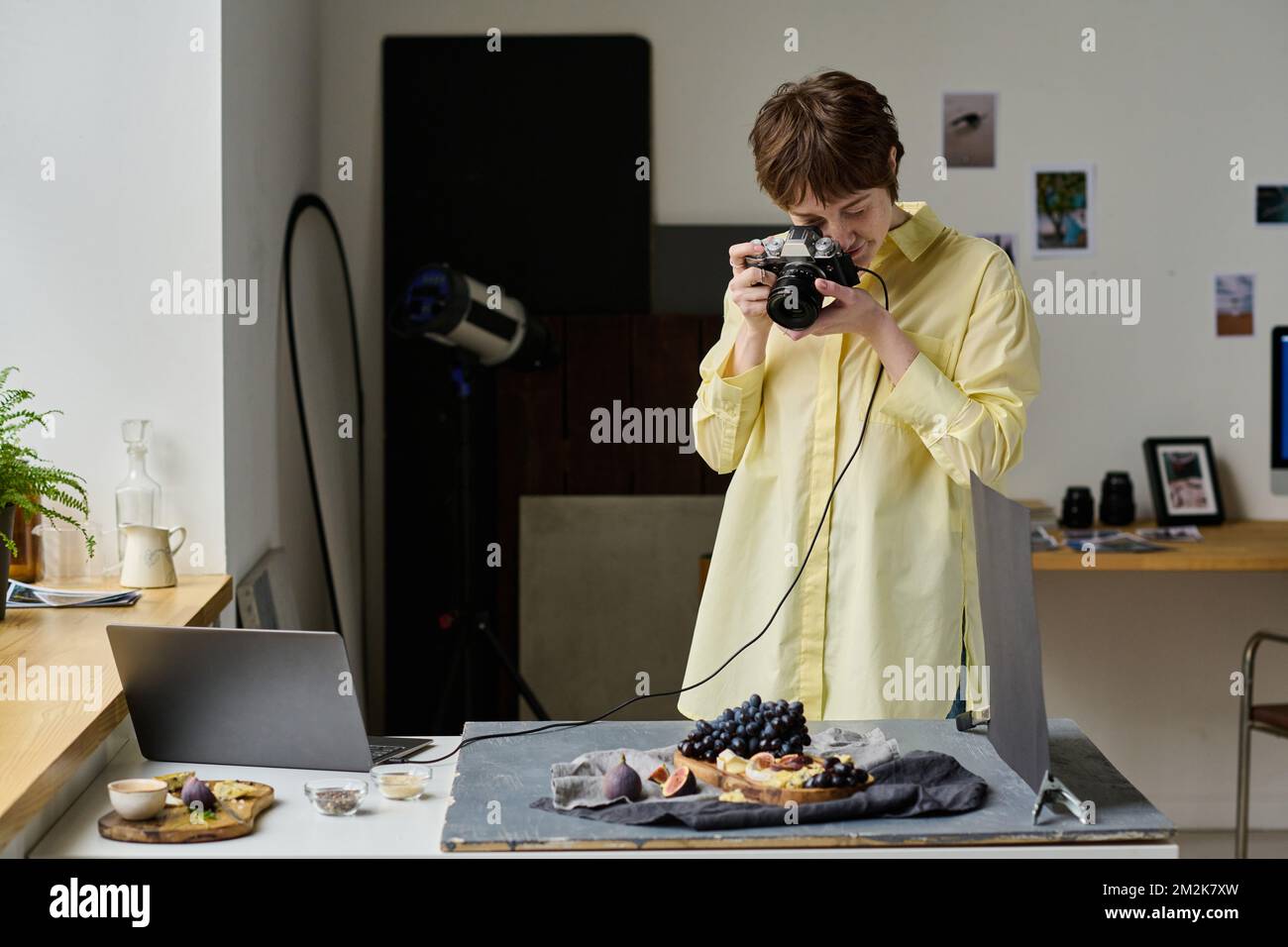 Jeune femme utilisant un appareil photo professionnel pour prendre des photos de fruits frais pendant son travail en studio photo Banque D'Images