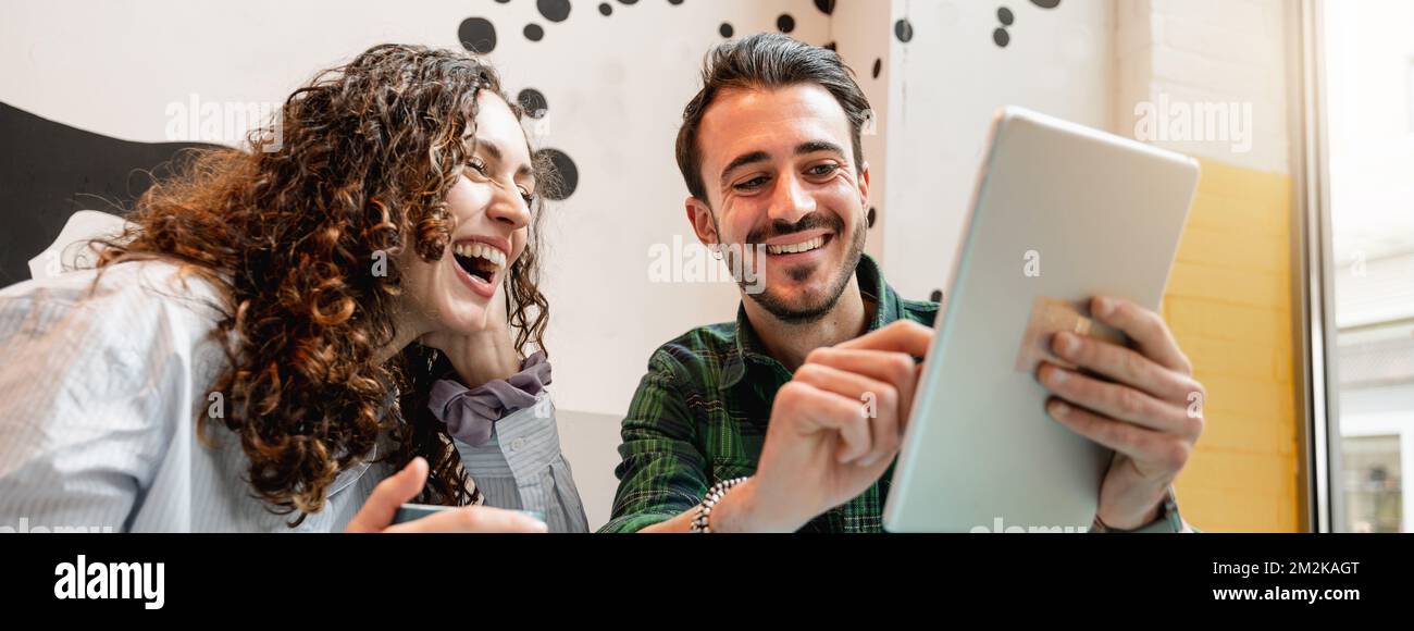 Restaurant riant regarder quelque chose à la tablette.bannière horizontale ou en-tête heureux jeune couple assis dans Banque D'Images