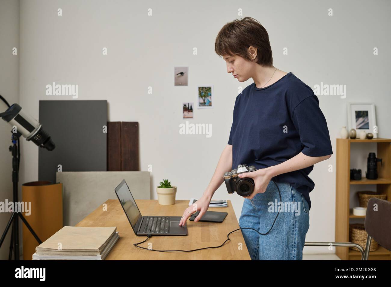 Jeune photographe connectant un appareil photo à un ordinateur portable pour regarder ses photos pendant son travail en studio Banque D'Images