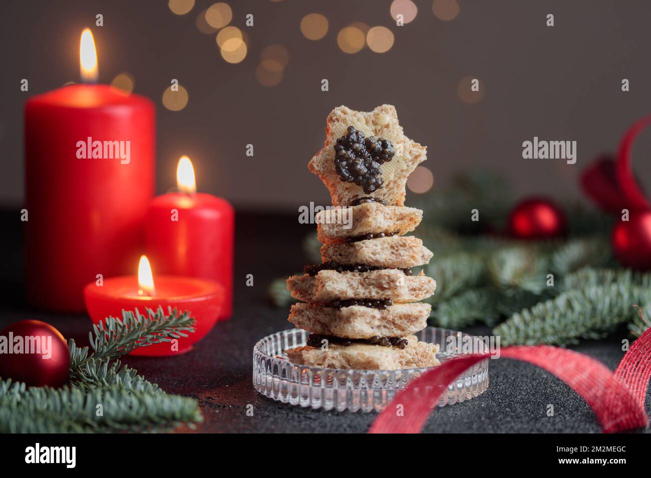Caviar noir hors-d'œuvre étoiles sur une table noire décorée de noël avec des bougies rouges et bokeh horizontal Banque D'Images